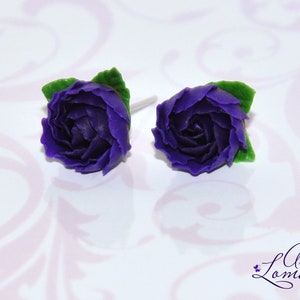 May include: A pair of purple flower stud earrings with green leaves. The earrings are made of polymer clay and are handmade.