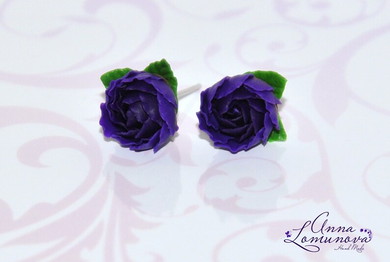 May include: A pair of purple flower stud earrings with green leaves. The earrings are made of polymer clay and are handmade.
