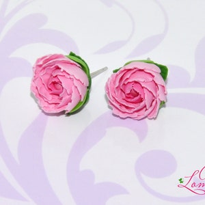 Pode incluir: Um par de brincos de argila polim&eacute;rica rosa em forma de rosas com folhas verdes. Os brincos est&atilde;o sobre um fundo branco com um padr&atilde;o floral.