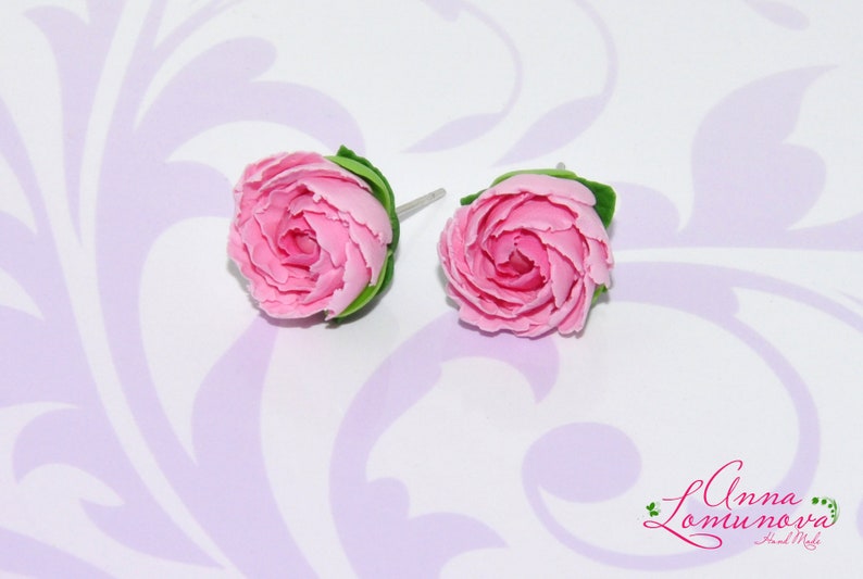 Pode incluir: Um par de brincos de argila polim&eacute;rica rosa em forma de rosas com folhas verdes. Os brincos est&atilde;o sobre um fundo branco com um padr&atilde;o floral.