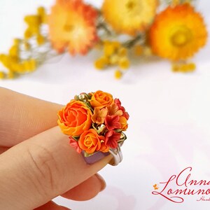 Peut inclure: Une bague orn&eacute;e d'un bouquet de fleurs en p&acirc;te polym&egrave;re orange et rouge. Les fleurs sont dispos&eacute;es en forme de bouquet et sont rehauss&eacute;es de paillettes dor&eacute;es.