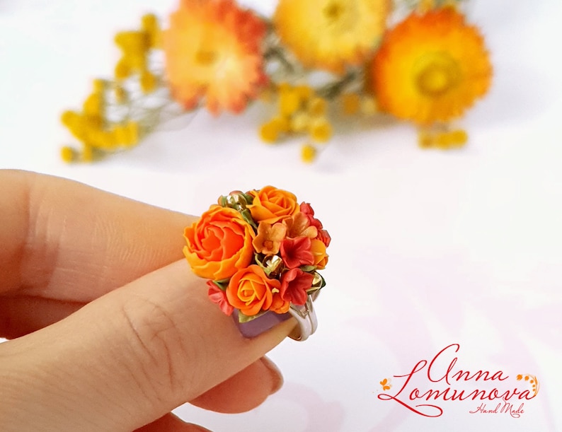Peut inclure: Une bague orn&eacute;e d'un bouquet de fleurs en p&acirc;te polym&egrave;re orange et rouge. Les fleurs sont dispos&eacute;es en forme de bouquet et sont rehauss&eacute;es de paillettes dor&eacute;es.
