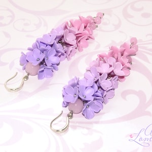 Peut inclure: Une paire de boucles d'oreilles longues et pendantes avec un d&eacute;grad&eacute; de fleurs violettes et roses. Les boucles d'oreilles sont en p&acirc;te polym&egrave;re et ont un crochet argent&eacute;.