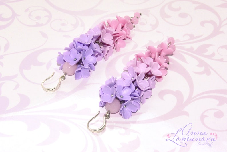 Peut inclure: Une paire de boucles d'oreilles longues et pendantes avec un d&eacute;grad&eacute; de fleurs violettes et roses. Les boucles d'oreilles sont en p&acirc;te polym&egrave;re et ont un crochet argent&eacute;.