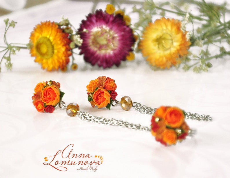 Peut inclure: Une paire de boucles d'oreilles en fleurs orange et rouge avec des cha&icirc;nes argent&eacute;es et des perles de cristal transparentes. Les boucles d'oreilles sont faites &agrave; la main et pr&eacute;sentent un motif floral d&eacute;licat.