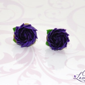May include: A pair of purple polymer clay earrings shaped like roses with green leaves.