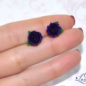 May include: A pair of purple flower earrings with green leaves. The earrings are made of polymer clay and are about 1 inch in diameter.