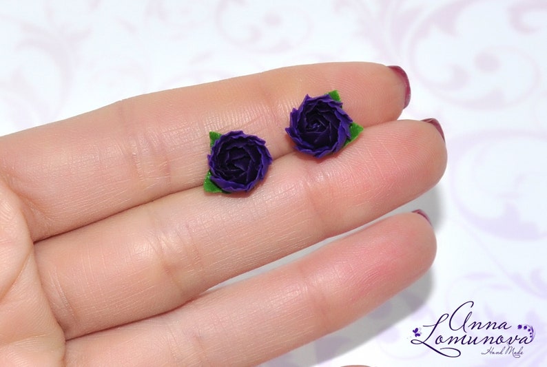 May include: A pair of purple flower earrings with green leaves. The earrings are made of polymer clay and are about 1 inch in diameter.