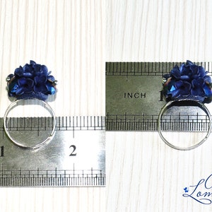 May include: A blue flower ring with a silver band. The ring is measured against a ruler, showing it is just under 1 inch in diameter.
