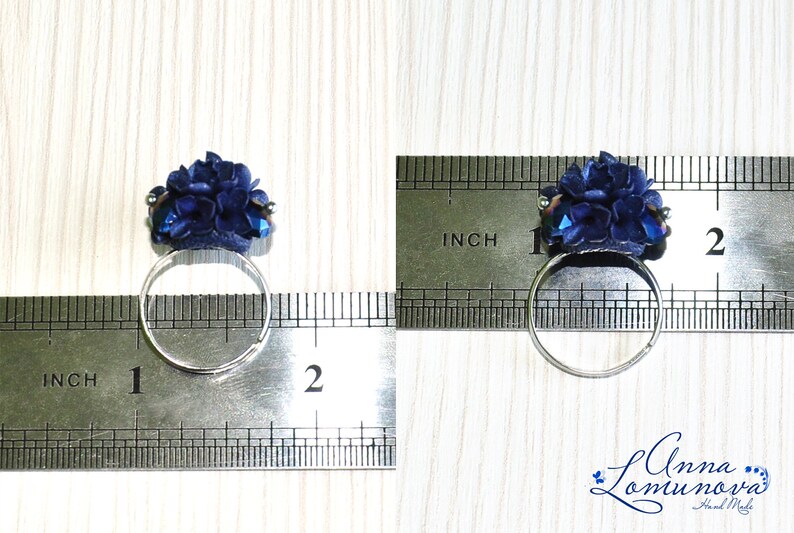 May include: A blue flower ring with a silver band. The ring is measured against a ruler, showing it is just under 1 inch in diameter.