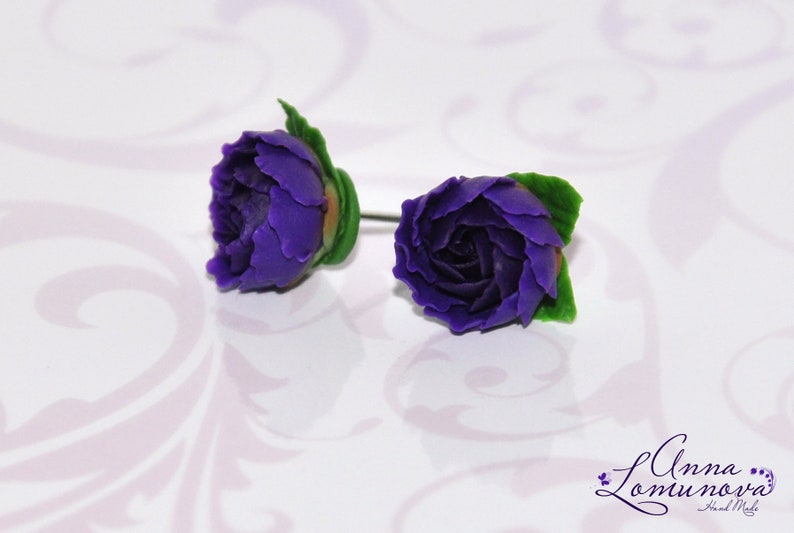 May include: A pair of purple flower earrings with green leaves. The earrings are made of polymer clay and are handmade.