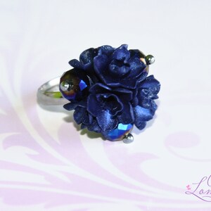 May include: A navy blue flower ring with iridescent crystal accents. The ring is made of silver metal.