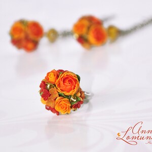 Peut inclure: Une bague orn&eacute;e d'un bouquet de fleurs en p&acirc;te polym&egrave;re orange et rouge. Les fleurs sont dispos&eacute;es en forme de bouquet et ont un aspect r&eacute;aliste.