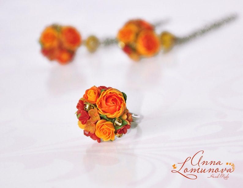 Peut inclure: Une bague orn&eacute;e d'un bouquet de fleurs en p&acirc;te polym&egrave;re orange et rouge. Les fleurs sont dispos&eacute;es en forme de bouquet et ont un aspect r&eacute;aliste.