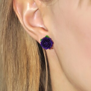 May include: Purple flower stud earrings with green leaves. The earrings are handmade and feature a delicate, realistic design.