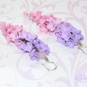 Peut inclure: Une paire de boucles d'oreilles pendantes avec un d&eacute;grad&eacute; de fleurs en p&acirc;te polym&egrave;re rose et violette. Les boucles d'oreilles sont attach&eacute;es &agrave; des crochets argent&eacute;s et ont une perle de quartz rose au bas.