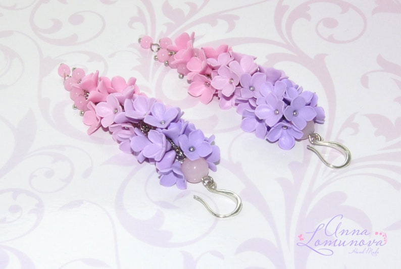 Peut inclure: Une paire de boucles d'oreilles pendantes avec un d&eacute;grad&eacute; de fleurs en p&acirc;te polym&egrave;re rose et violette. Les boucles d'oreilles sont attach&eacute;es &agrave; des crochets argent&eacute;s et ont une perle de quartz rose au bas.
