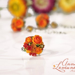 Peut inclure: Une bague orn&eacute;e d'un bouquet de fleurs en p&acirc;te polym&egrave;re orange et rouge. Les fleurs sont dispos&eacute;es en forme de bouquet et sont rehauss&eacute;es de feuilles vertes. La bague est r&eacute;alis&eacute;e par Anna Lomunova et est faite &agrave; la main.