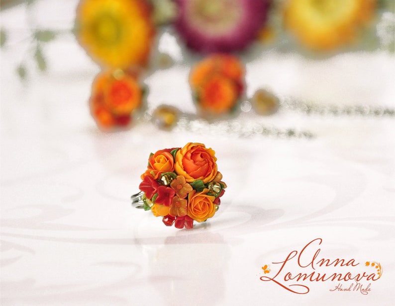 Peut inclure: Une bague orn&eacute;e d'un bouquet de fleurs en p&acirc;te polym&egrave;re orange et rouge. Les fleurs sont dispos&eacute;es en forme de bouquet et sont rehauss&eacute;es de feuilles vertes. La bague est r&eacute;alis&eacute;e par Anna Lomunova et est faite &agrave; la main.