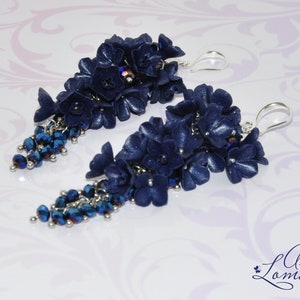 May include: A pair of long, dangling earrings with navy blue polymer clay flowers and crystal beads. The earrings have silver hooks.