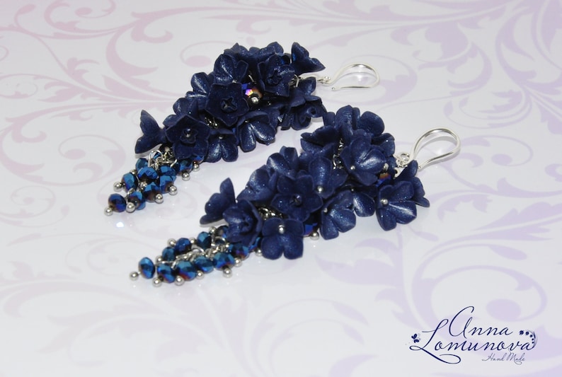 May include: A pair of long, dangling earrings with navy blue polymer clay flowers and crystal beads. The earrings have silver hooks.