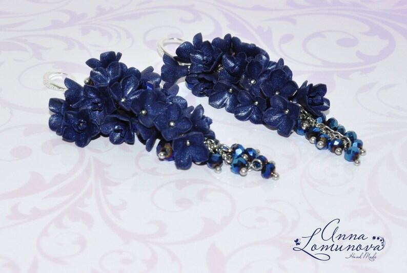 May include: A pair of dangle earrings with a cluster of dark blue polymer clay flowers and a silver chain with dark blue crystal beads.