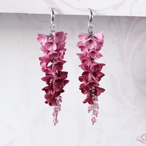 May include: A pair of dangle earrings with a gradient of pink and red polymer clay flowers. The flowers are arranged in a cascading design and are accented with small pink crystal beads.