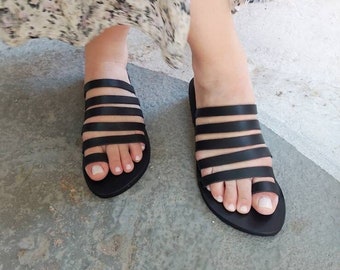 May include: Black leather sandals with multiple straps. The sandals have a simple design and are perfect for summer.
