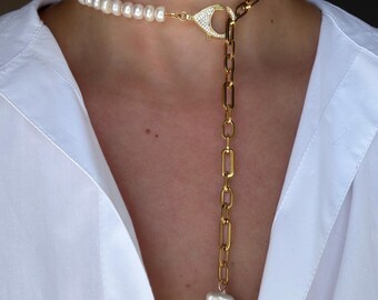 May include: A two-strand necklace featuring white pearls and gold-toned chain links. The top strand is a choker of small pearls, while the second strand has a gold chain that dangles down to a large, irregular white pearl pendant.