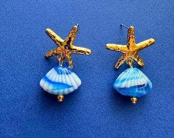 Könnte beinhalten: Goldene Seestern-Ohrringe mit blauen und weißen Glasmuschel-Anhängern.