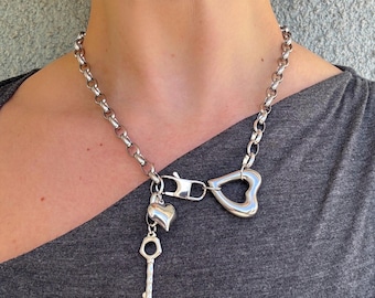 May include: Silver necklace with a chunky chain. It features a heart-shaped pendant, a small heart charm, and a key charm. The necklace is secured with a clasp.