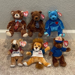 May include: Six plush stuffed animals, all brown bears except for one blue bear. The bears are wearing various outfits, including a tie, a blue shirt, and a red shirt. The bears are all holding Ty tags. The bears are arranged in a row on a clear plastic shelf.