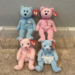 May include: Four plush teddy bears, two blue and two pink, with embroidered details. The blue bears have "It's a Boy" and "Baby" embroidered on them, while the pink bears have "It's a Girl" and "Baby" embroidered on them. The bears are all wearing diaper-like fabric around their waists.