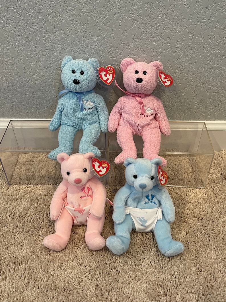 May include: Four plush teddy bears, two blue and two pink, with embroidered details. The blue bears have "It's a Boy" and "Baby" embroidered on them, while the pink bears have "It's a Girl" and "Baby" embroidered on them. The bears are all wearing diaper-like fabric around their waists.
