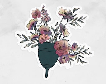 May include: A dark blue menstrual cup surrounded by a bouquet of pink, purple, and white flowers with green stems and leaves.