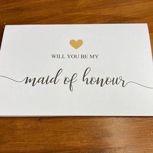 Puede incluir: Tarjeta blanca con un coraz&oacute;n dorado y texto negro que dice "&iquest;Quieres ser mi dama de honor?"