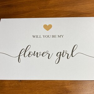Puede incluir: Tarjeta blanca con un coraz&oacute;n dorado y el texto "&iquest;Quieres ser mi dama de honor?" en escritura cursiva negra.
