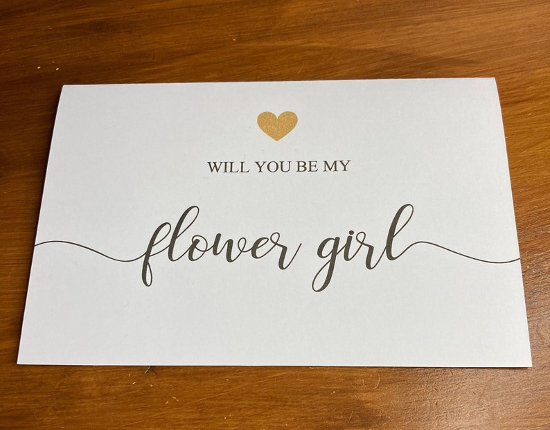 Puede incluir: Tarjeta blanca con un coraz&oacute;n dorado y el texto "&iquest;Quieres ser mi dama de honor?" en escritura cursiva negra.