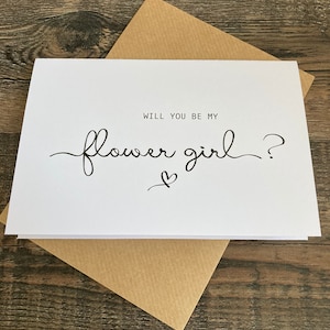 May include: White card with black text that reads "Will you be my flower girl?" with a small heart symbol.