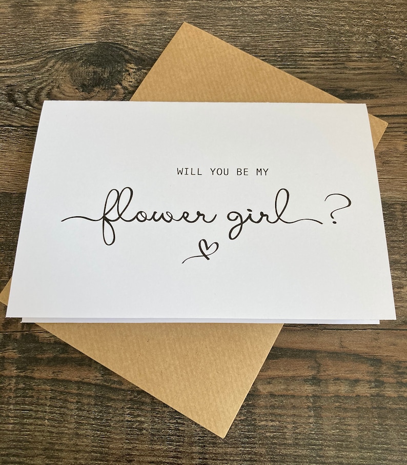 May include: White card with black text that reads "Will you be my flower girl?" with a small heart symbol.