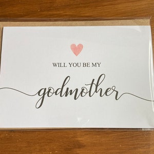 May include: White card with a pink heart and the text "Will you be my godmother" in black cursive writing.