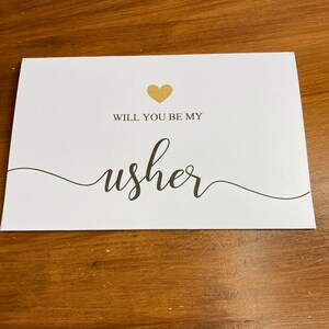 Puede incluir: Tarjeta blanca con un coraz&oacute;n dorado y el texto "&iquest;Quieres ser mi padrino?" en escritura cursiva negra.