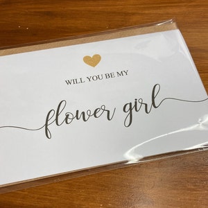 Puede incluir: Tarjeta blanca con un coraz&oacute;n dorado y el texto "&iquest;Quieres ser mi dama de honor?" en letra negra.