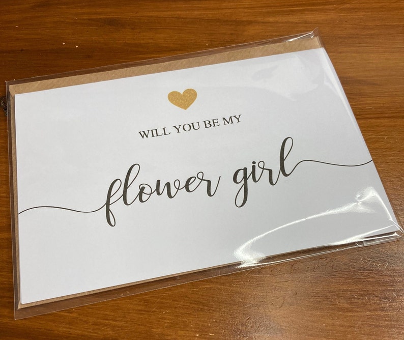 Puede incluir: Tarjeta blanca con un coraz&oacute;n dorado y el texto "&iquest;Quieres ser mi dama de honor?" en letra negra.