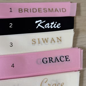 May include: Close-up of personalized ribbons in various colors, including pink, black, and cream. The ribbons display names and titles in different fonts, such as "Bridesmaid," "Katie," "Siwan," and "Grace." The text "Font Style" is at the top.