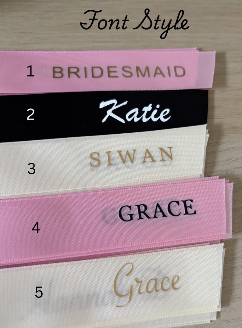 May include: Close-up of personalized ribbons in various colors, including pink, black, and cream. The ribbons display names and titles in different fonts, such as "Bridesmaid," "Katie," "Siwan," and "Grace." The text "Font Style" is at the top.