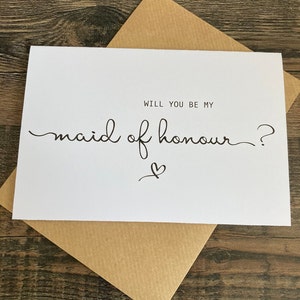 May include: White card with black text that reads "Will you be my maid of honour?" with a small heart symbol.
