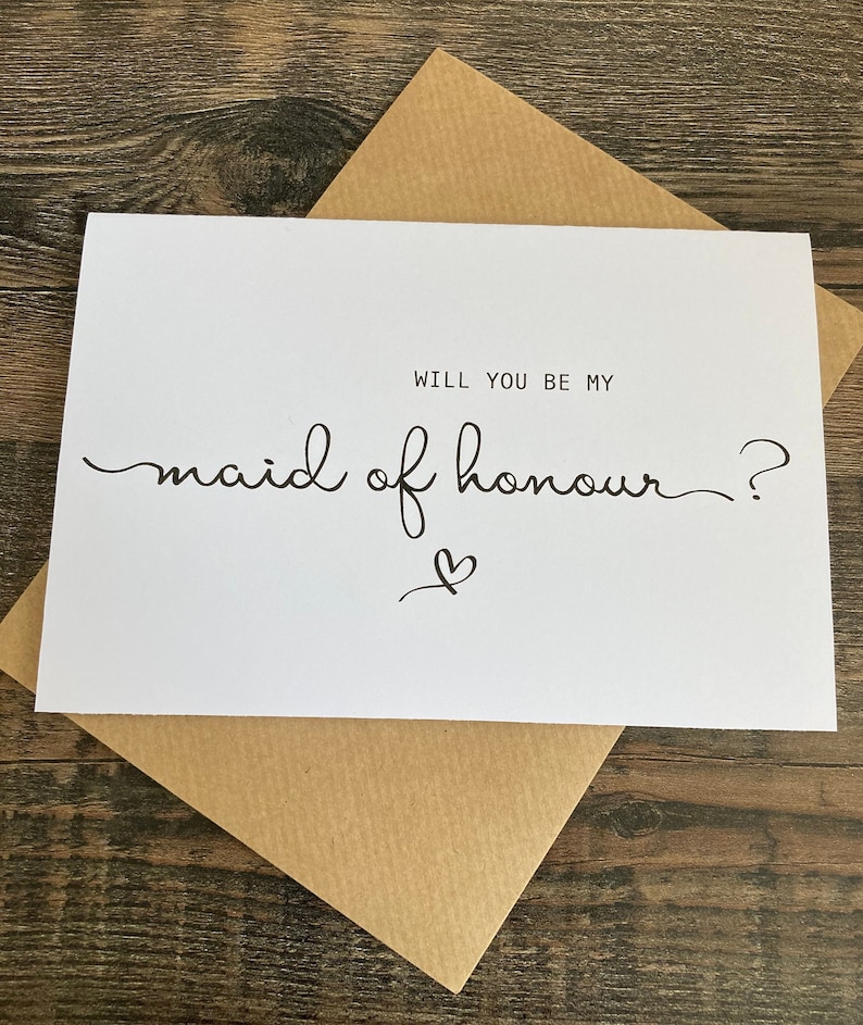 May include: White card with black text that reads "Will you be my maid of honour?" with a small heart symbol.