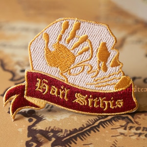May include: A white and gold embroidered patch with a handprint design and the text "Barry Sitris" on a red banner.