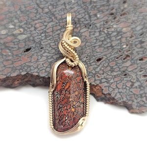 May include: A gold-colored pendant with a rectangular, patterned stone. The stone features a mix of red, brown, and yellow hues with a unique, textured pattern. The pendant is wire-wrapped and has a loop for a chain.